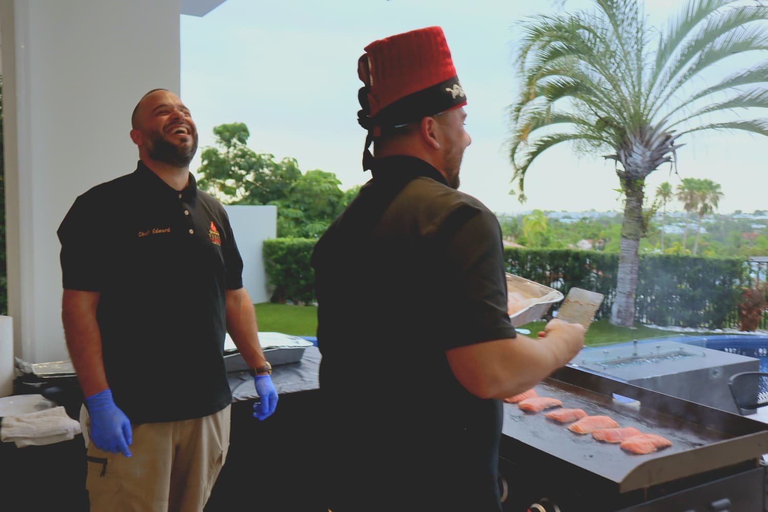 Los chefs Edward y Dexler riendo durante un evento con salmón en la plancha